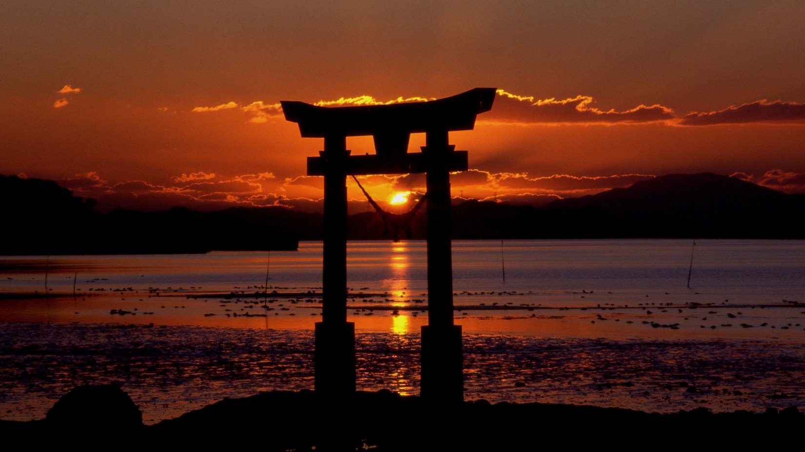 A torii gate silhouetted against a sunset over the water