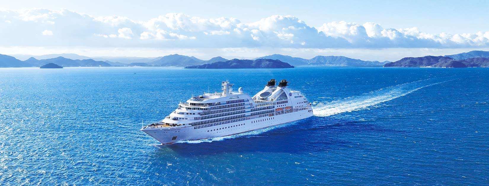 A cruise ship sailing between islands on a blue sea