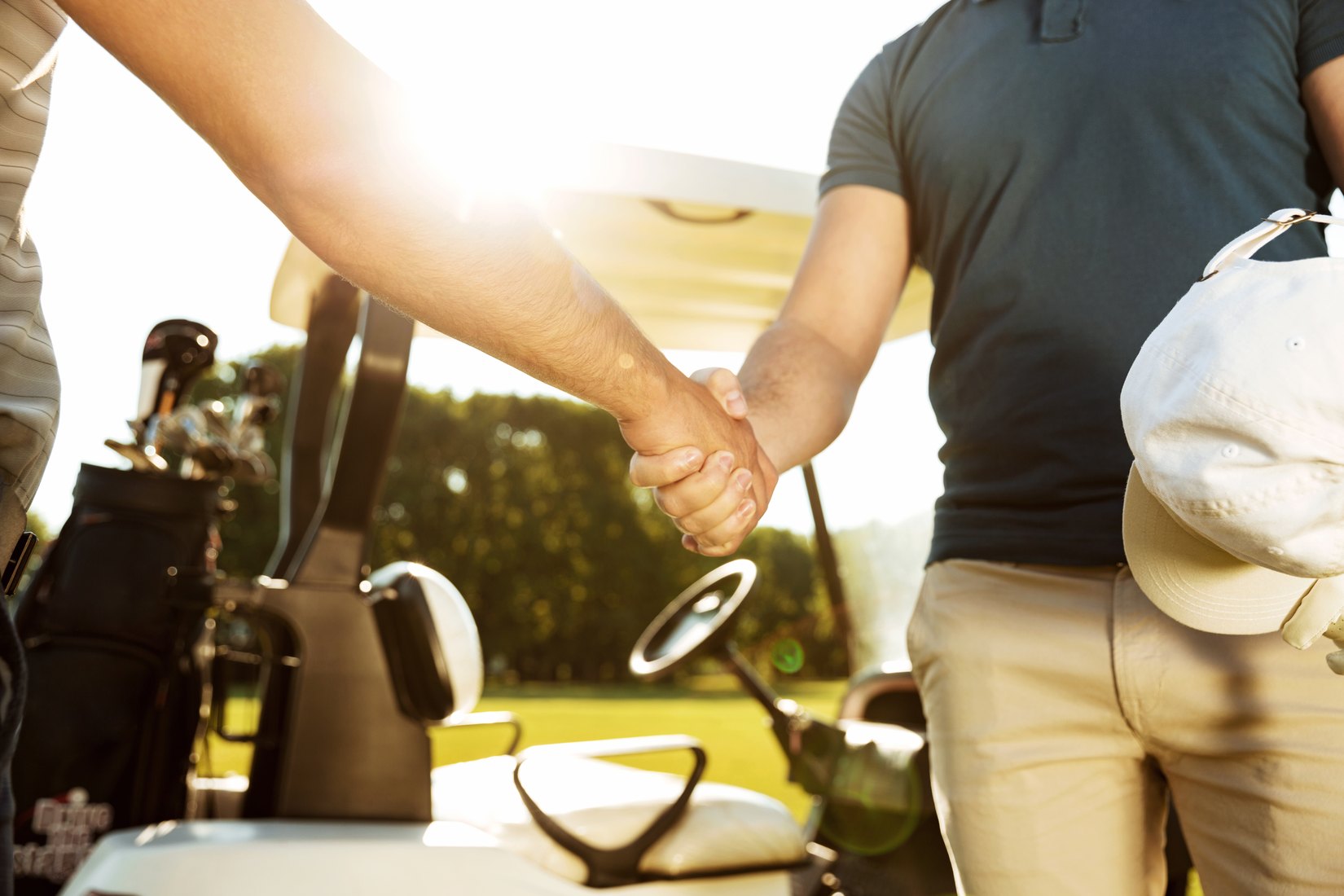Golfers shaking hands beside a golf cart